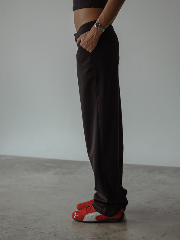 Vista lateral de modelo con una mano en el bolsillo, usando un pantalón clásico color negro con bolsillos laterales y bota recta, combinado con un top asimétrico color negro.