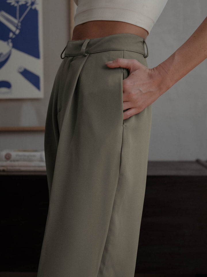 Vista a detalle de pantalón plisado color gris con bolsillos laterales.