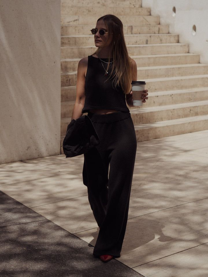 Modelo usando un pantalón tejido color negro de silueta ancha y un crop top tejido color negro