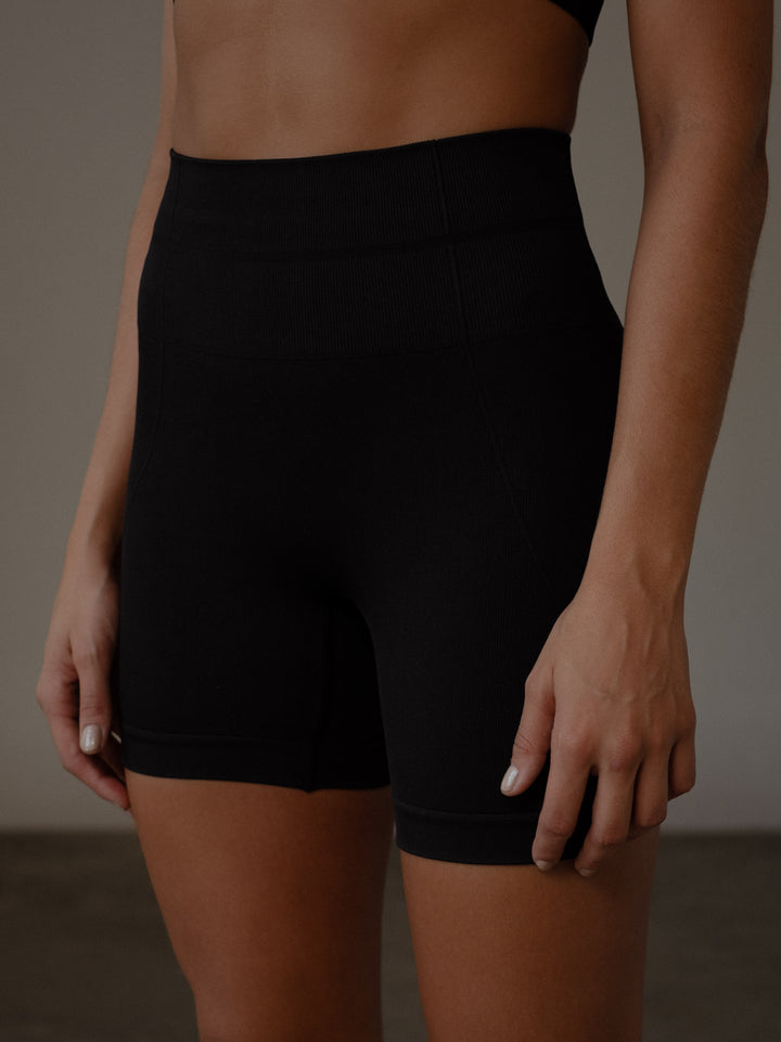Vista lateral de los shorts deportivos color negro con pretina acanalada doble y compresión en el abdomen