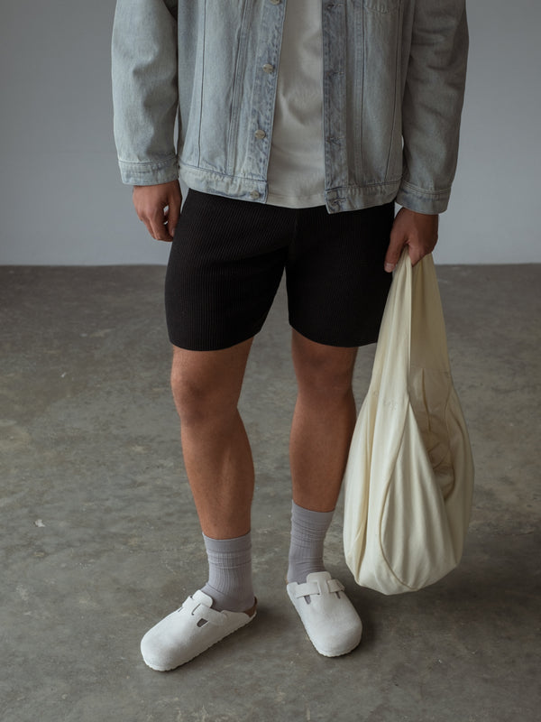 Modelo sosteniendo un bolso amarillo mientras usa medias grises y short tejido negro.