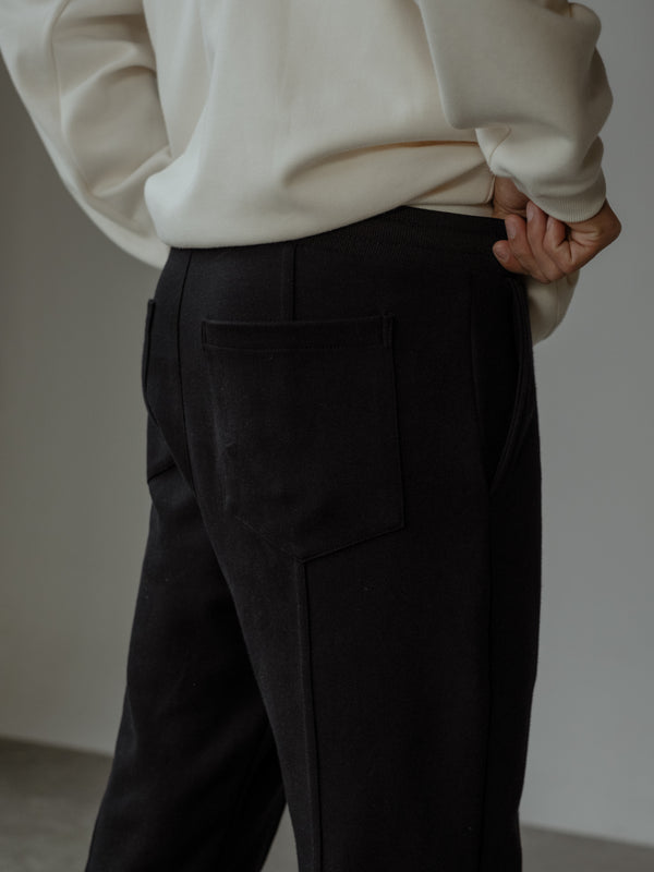 Detalle de la parte trasera de un pantalón color negro con bolsillo posterior, y un buzo color crema.