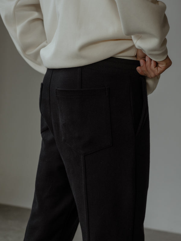 Detalle de la parte trasera de un pantalón color negro con bolsillo posterior, y un buzo color crema.