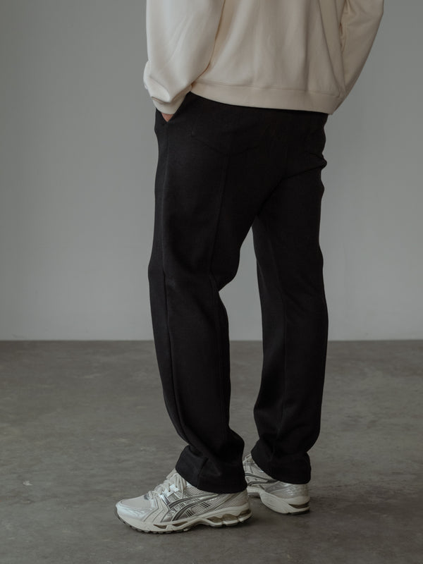 Modelo de espaldas con las manos en los bolsillos, usando un pantalón de color negro y un buzo color crema.