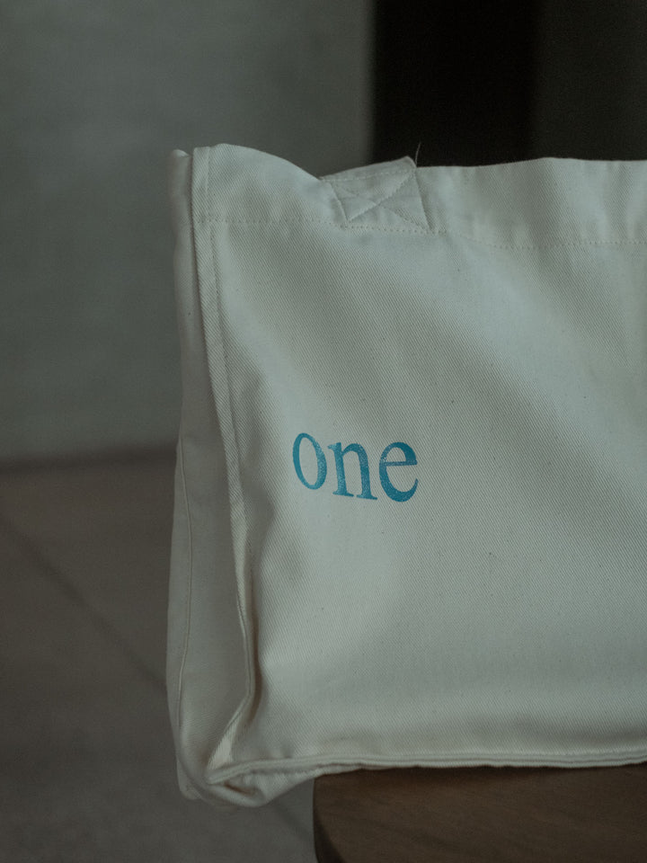 Vista detallada del estampado "One Half" en color azul cielo en el bolso color crudo