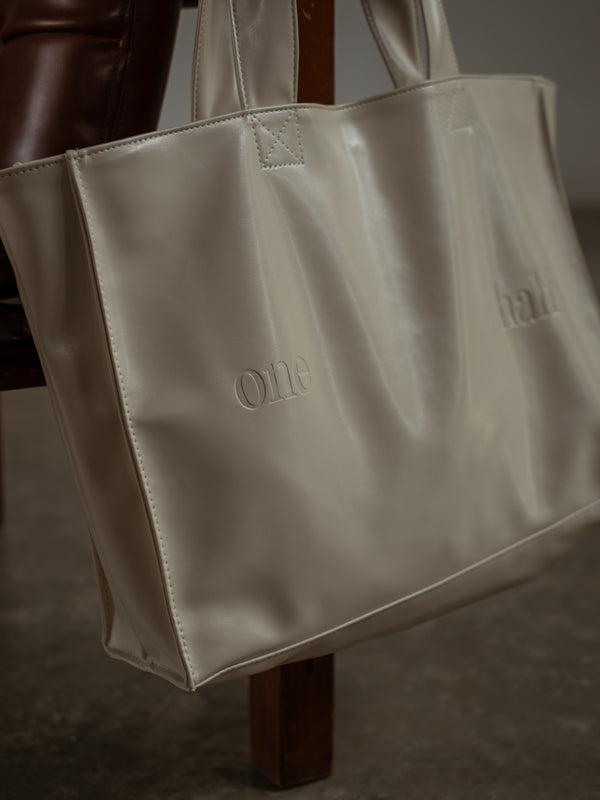 Tote bag color crema diseñada en cuero sintético con "One Half" grabado en la parte frontal