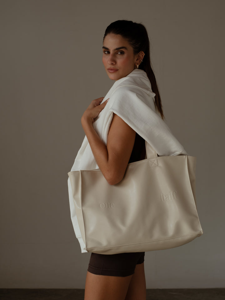 Vista lateral de la modelo usando un tote bag color crema en cuerina