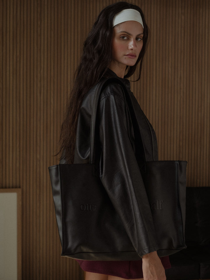 Vista lateral de la modelo usando una tote bag color negro en cuero sintético 