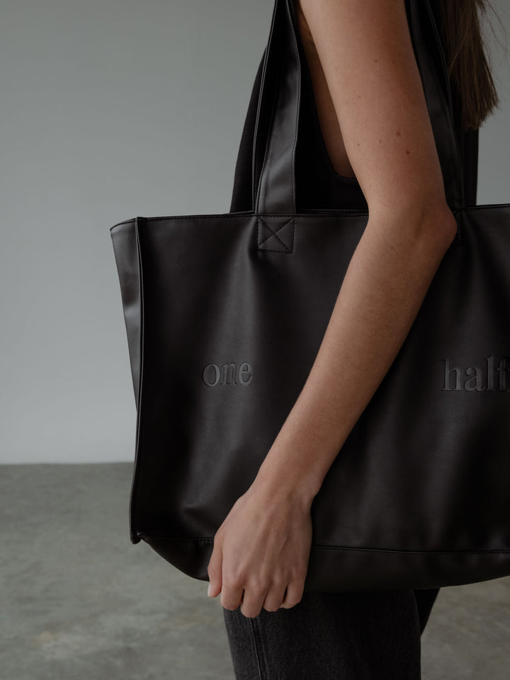 Tote bag color negro en cuero sintético con "One Half" grabado en la parte frontal