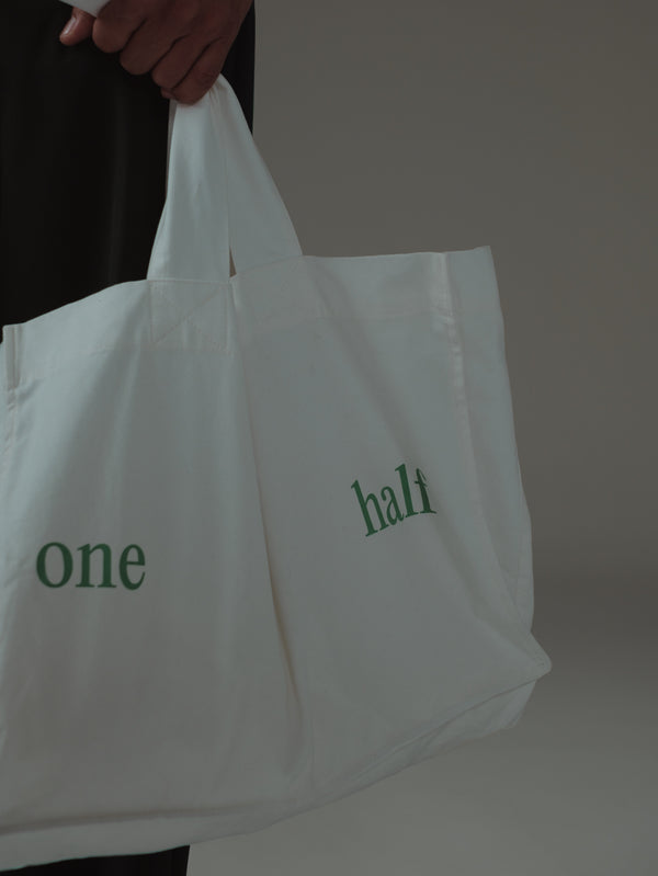 Vista frontal de tote bag crudo con estampado "One Half" en verde.