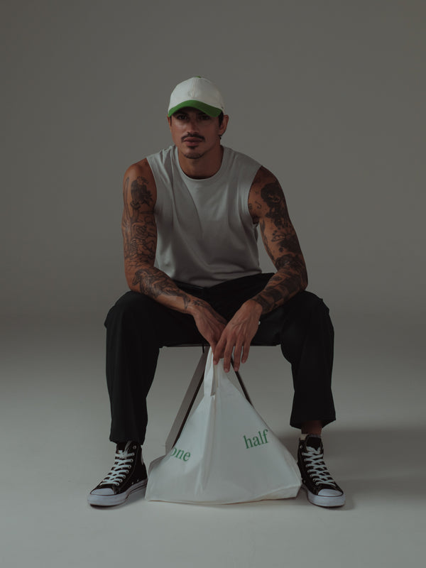 Modelo sentado con tank gris y pantalón negro sosteniendo tote bag.