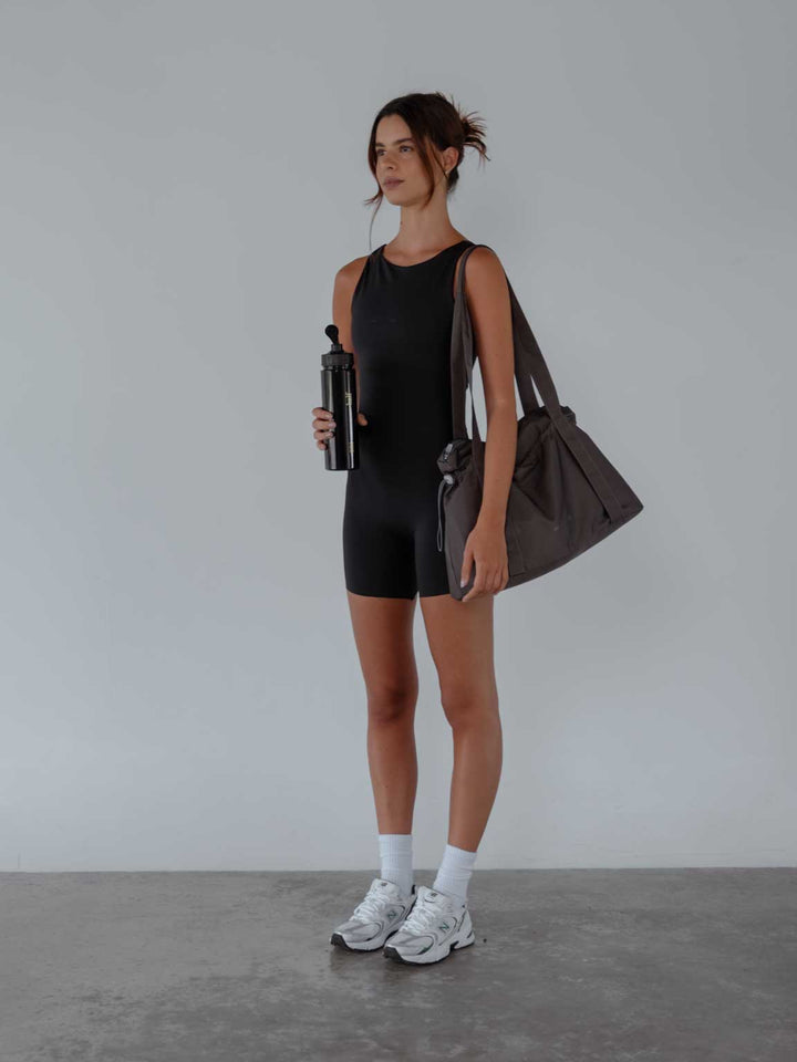  Vista completa de la modelo usando enterizo short color negro para mujer con bolso gris y termo.