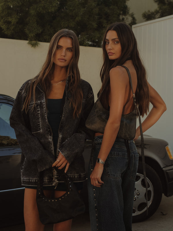 Dos modelos posando con chaqueta y vestido negro y top con jean azul.