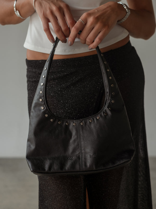 Modelo sosteniendo mini bolso negro de cuero sintético con taches.