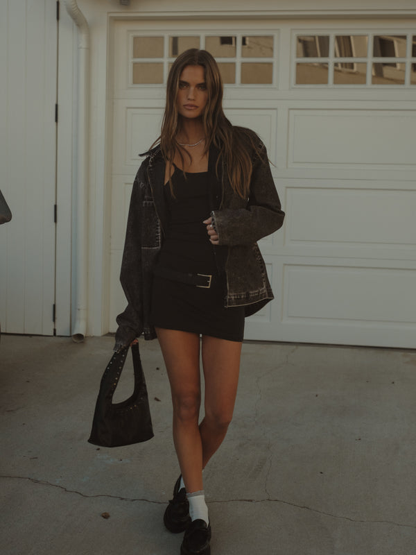 Modelo usando mini vestido negro con chaqueta y mini bolso negro.