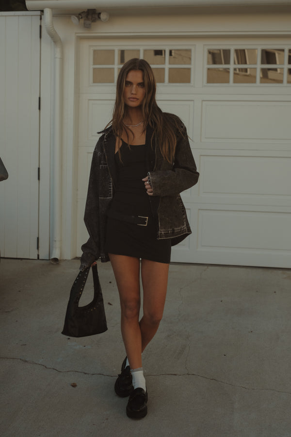 Modelo usando mini vestido negro con chaqueta y mini bolso negro.