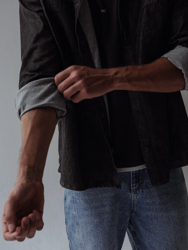 Vista a detalle de manga de camisa negra doblada tres cuartos.