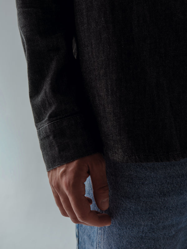 Vista a detalle de puño de manga larga de camisa negra denim. 