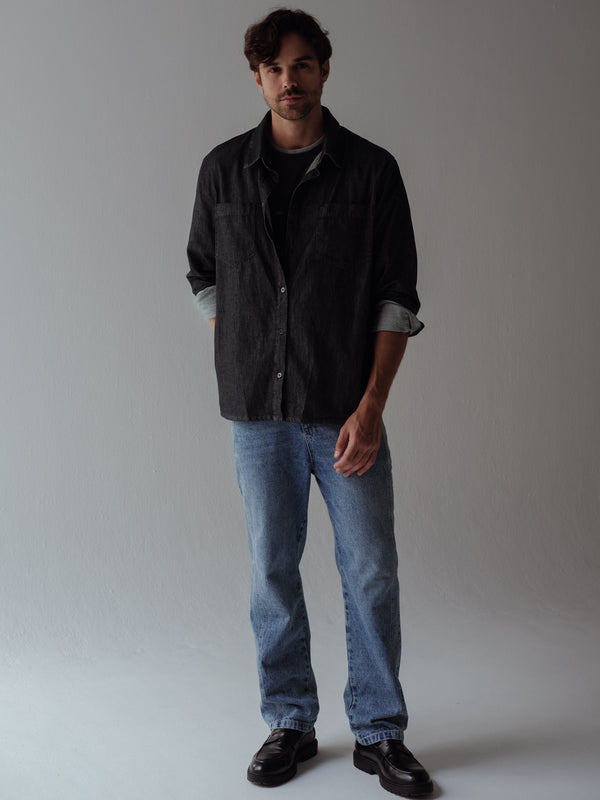 Modelo con jean clásico azul, camisa negra con lavado vintage y zapatos negros. 