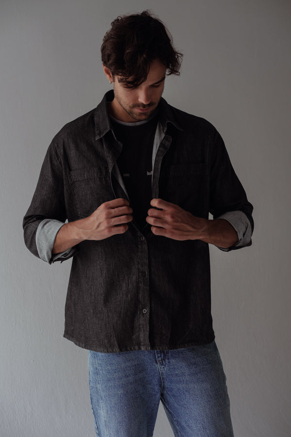 Modelo con camisa negra sobrepuesta con camiseta negra y jean azul.