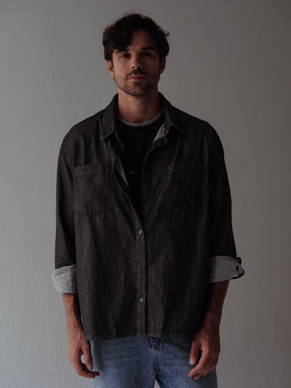 Modelo usando camisa denim negra manga doblada con jean azul.