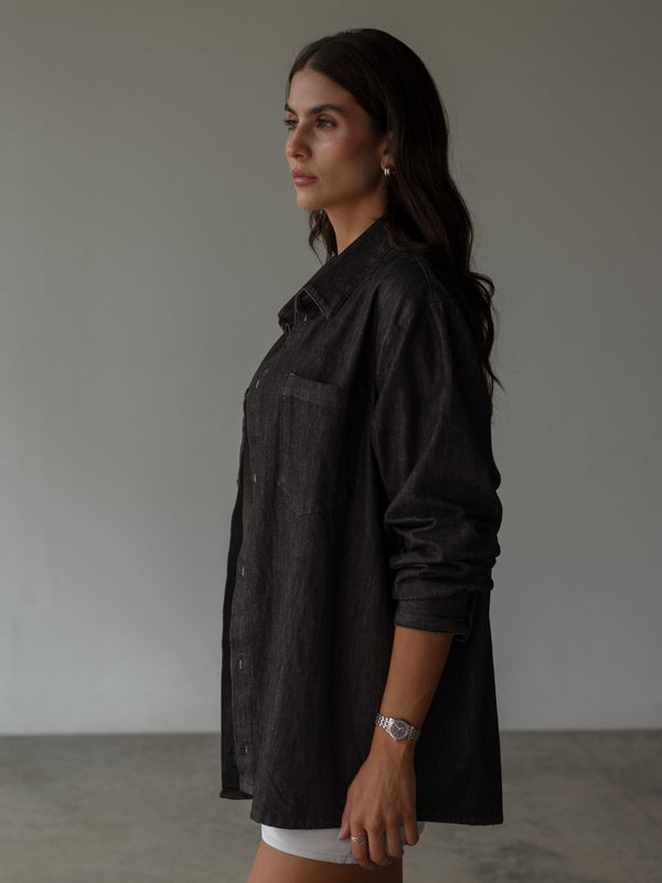 Vista lateral de camisa negra denim oversized con bolsillo y botones. 