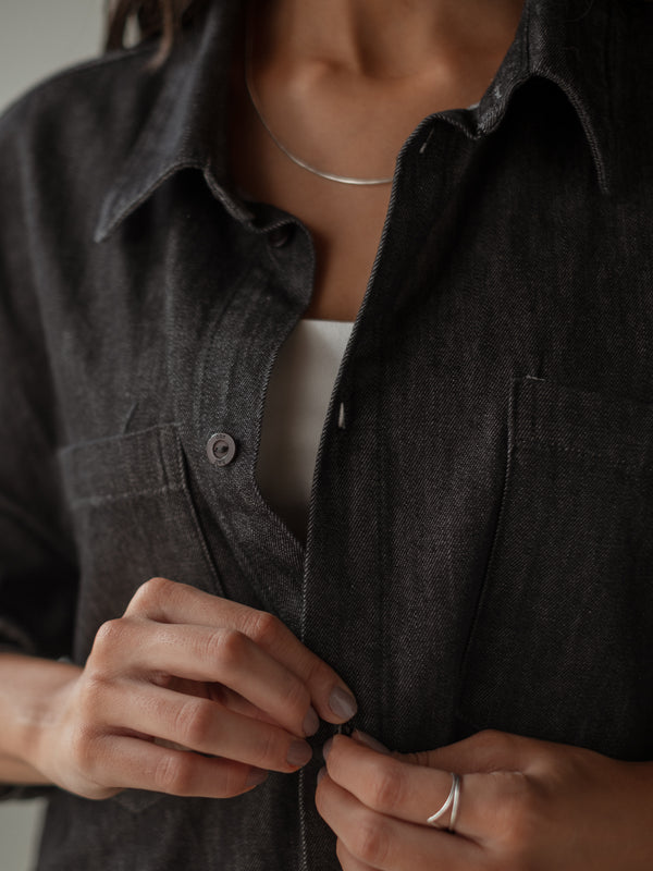 Vista a detalle botones de camisa negra denim con bolsillo frontal. 
