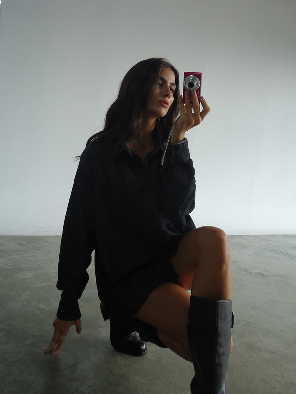 Modelo agachada tomando una foto en espejo usando camisa negra denim. 