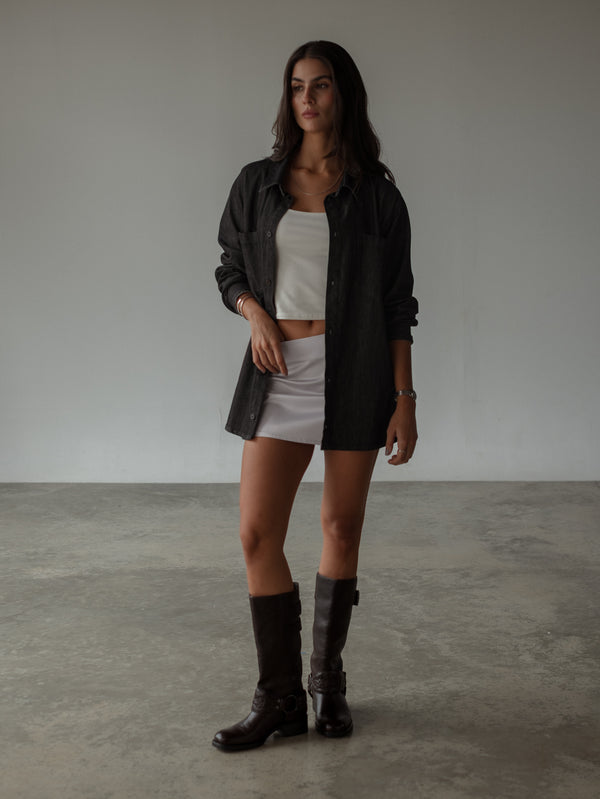 Modelo con top blanco, falda satinada, camisa negra oversized y botas. 