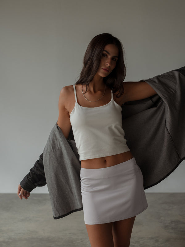 Modelo usando crop top blanco con falda gris con camisa negra abierta. 