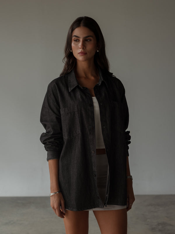 Modelo usando camisa negra oversized encima de top y falda.