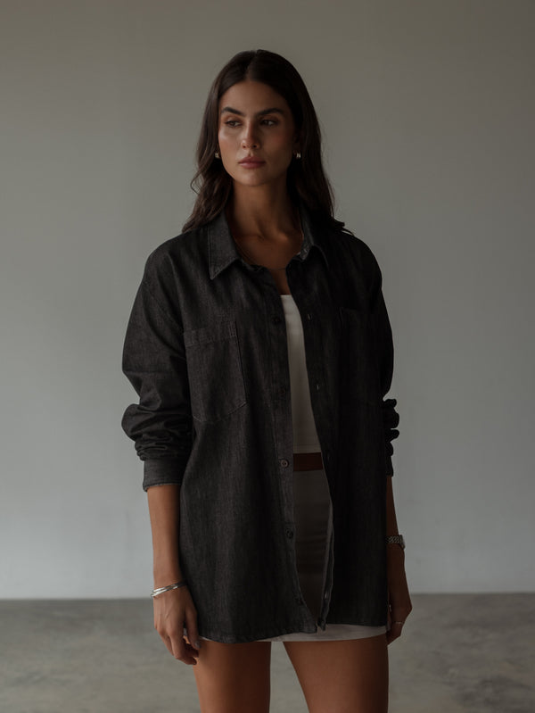 Modelo usando camisa negra oversized encima de top y falda.