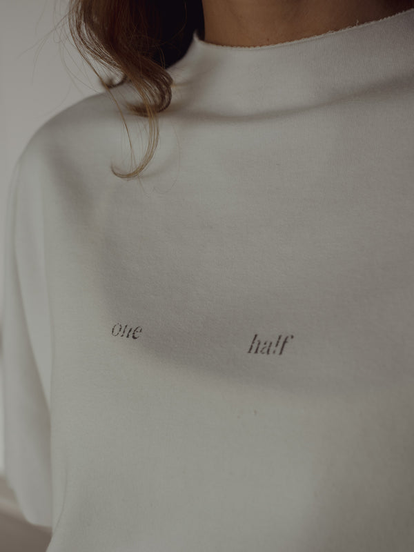 Vista a detalle estampado frontal "One Half" de camiseta crudo.