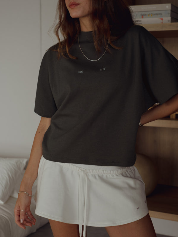 Vista frontal modelo usando camiseta gris oscuro con mini falda crudo.