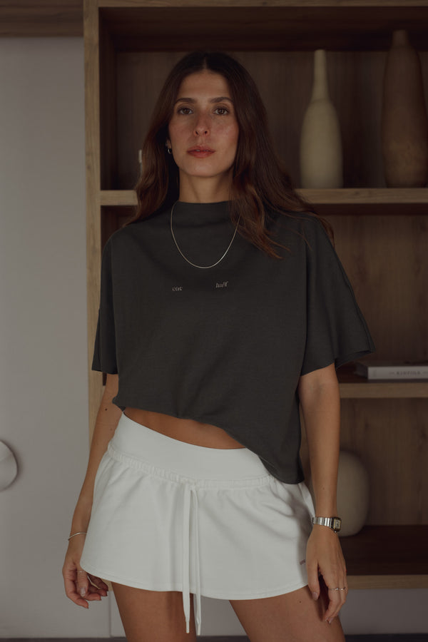 Vista frontal modelo usando camiseta gris oversized con mini falda crudo.