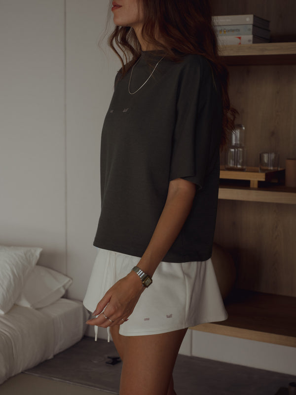 Modelo con camiseta gris al corte y mini falda crudo pretina ajustable.