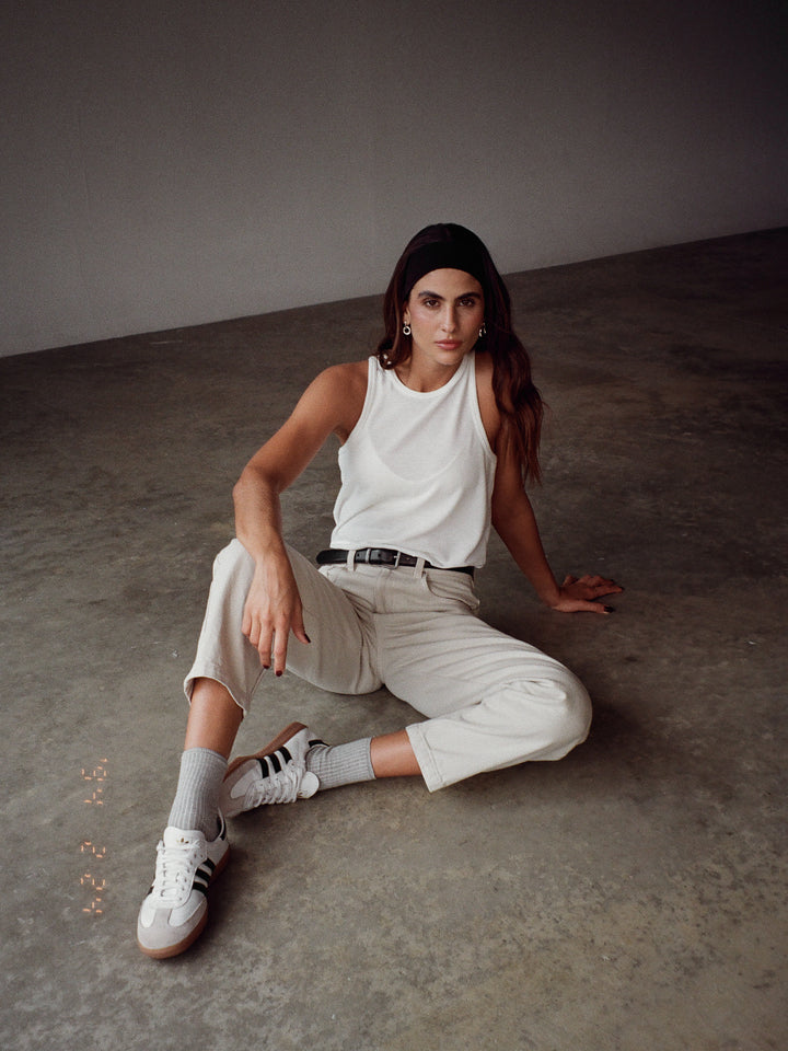 Modelo sentada en el suelo usando una camiseta blanca y jean