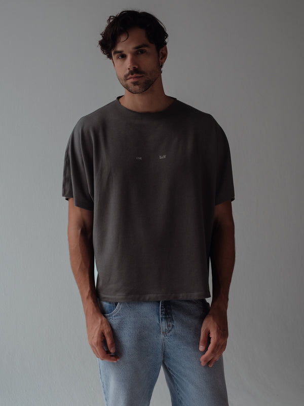 Modelo usando camiseta gris con detalles al corte y jean azul.