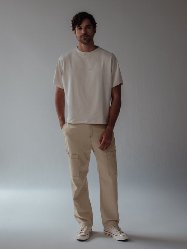 Modelo usando camiseta crema con jean tipo cargo y tenis claros. 