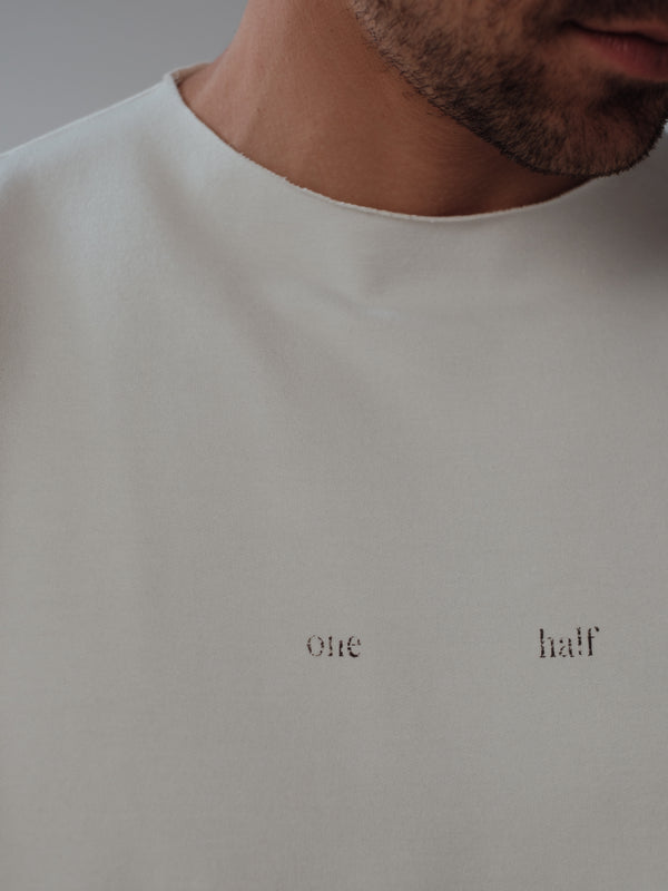 Vista a detalle cuello al corte y estampado "One Half" con desgaste camiseta crema.