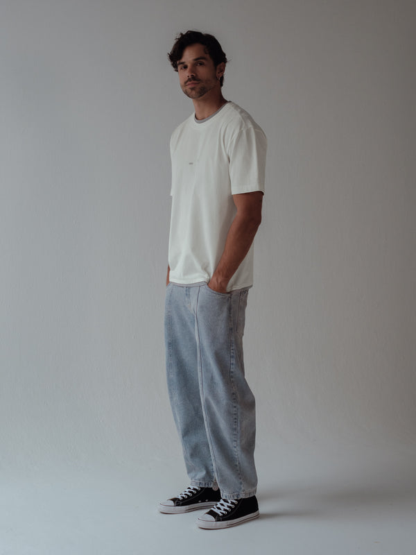 Modelo usando jean ancho azul claro con camiseta crudo y tenis negros. 