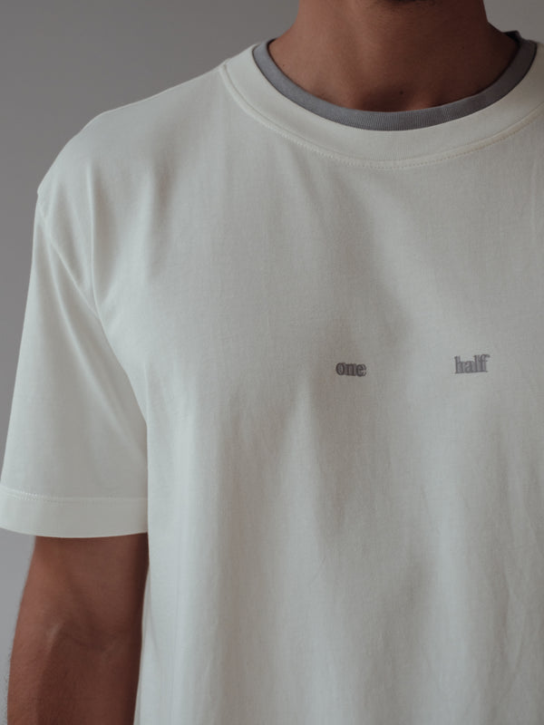 Vista a detalle camiseta crudo con doble cuello en gris y estampado "One Half". 