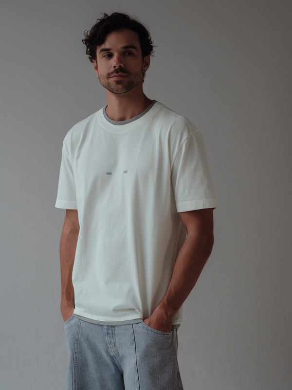 Modelo usando camiseta crudo con doble cuello y ruedo en gris.