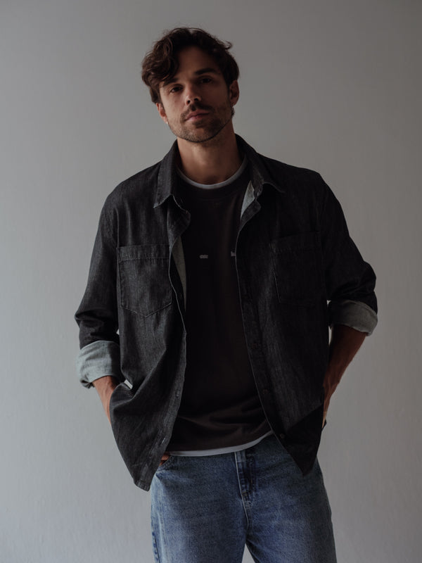 Modelo usando camisa negra abierta sobre camiseta negra con jean azul. 