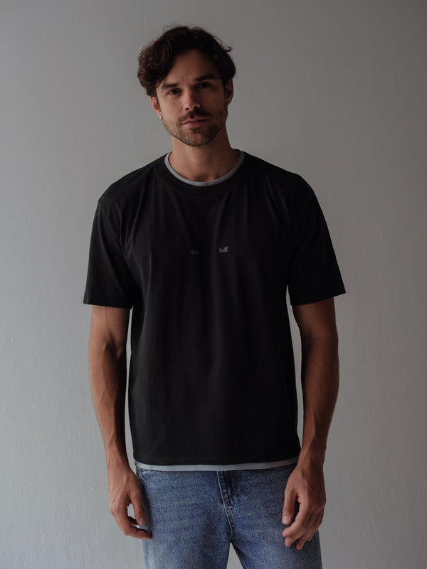 Modelo con camiseta negra regular con cuello y ruedo doble gris. 