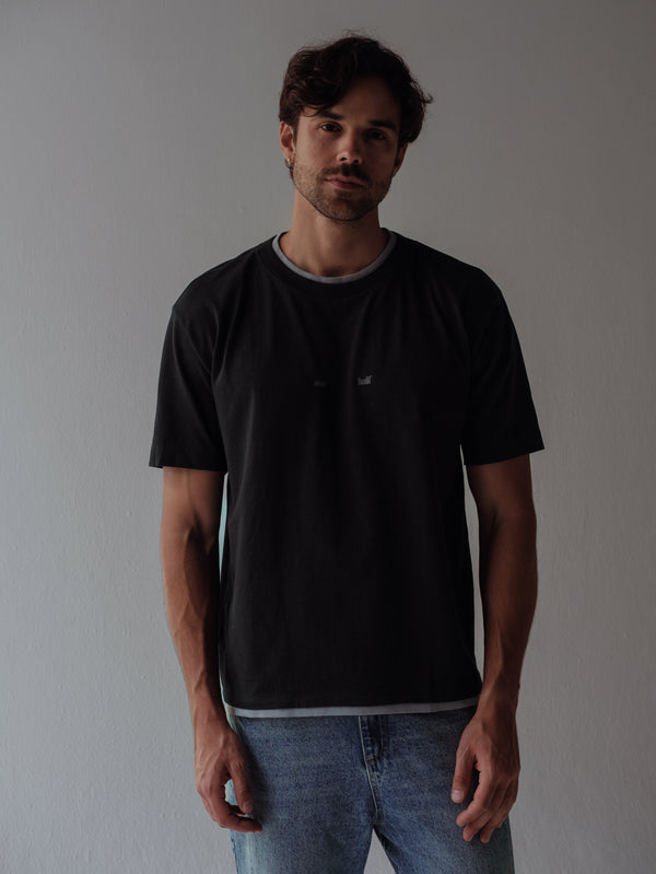 Modelo usando camiseta negra con doble contraste gris en cuello y ruedo.