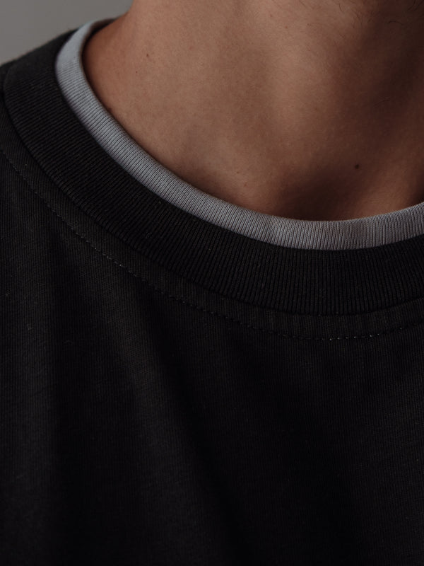 Vista a detalle camiseta negra con doble contraste en cuello color gris.