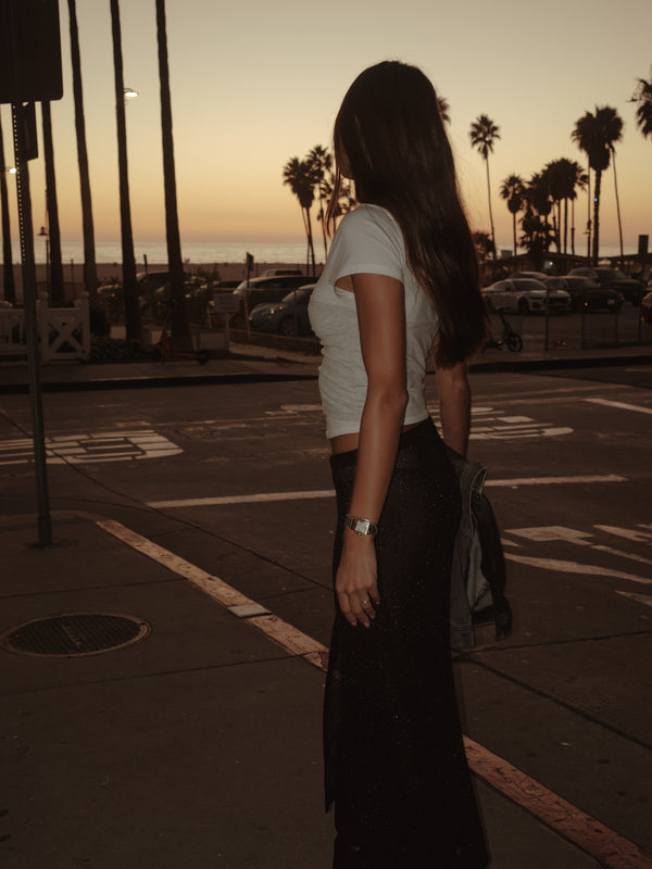 Vista lateral modelo con falda negra y camiseta crudo y gris tipo strapless.