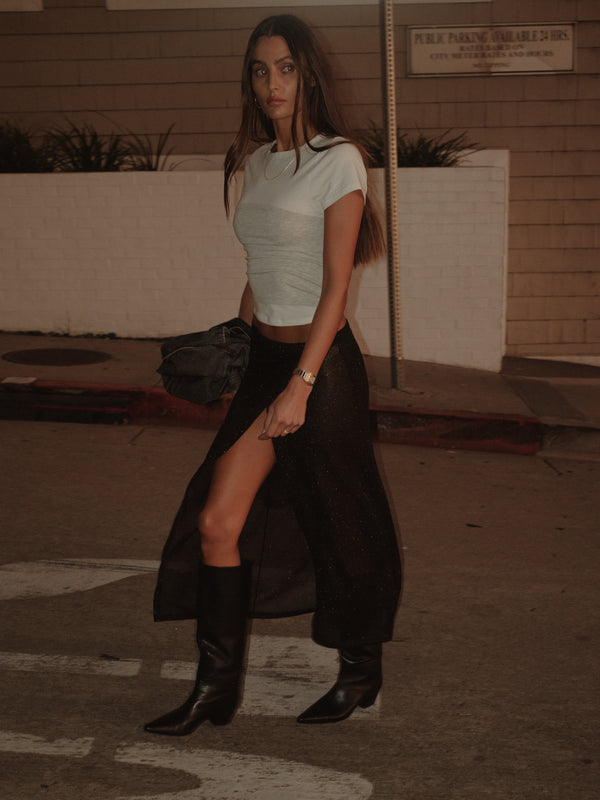 Modelo caminando con falda negra y camiseta crudo con strapless gris.