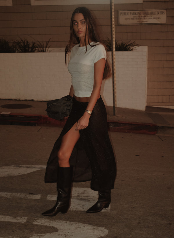 Modelo caminando con falda negra y camiseta crudo con strapless gris.